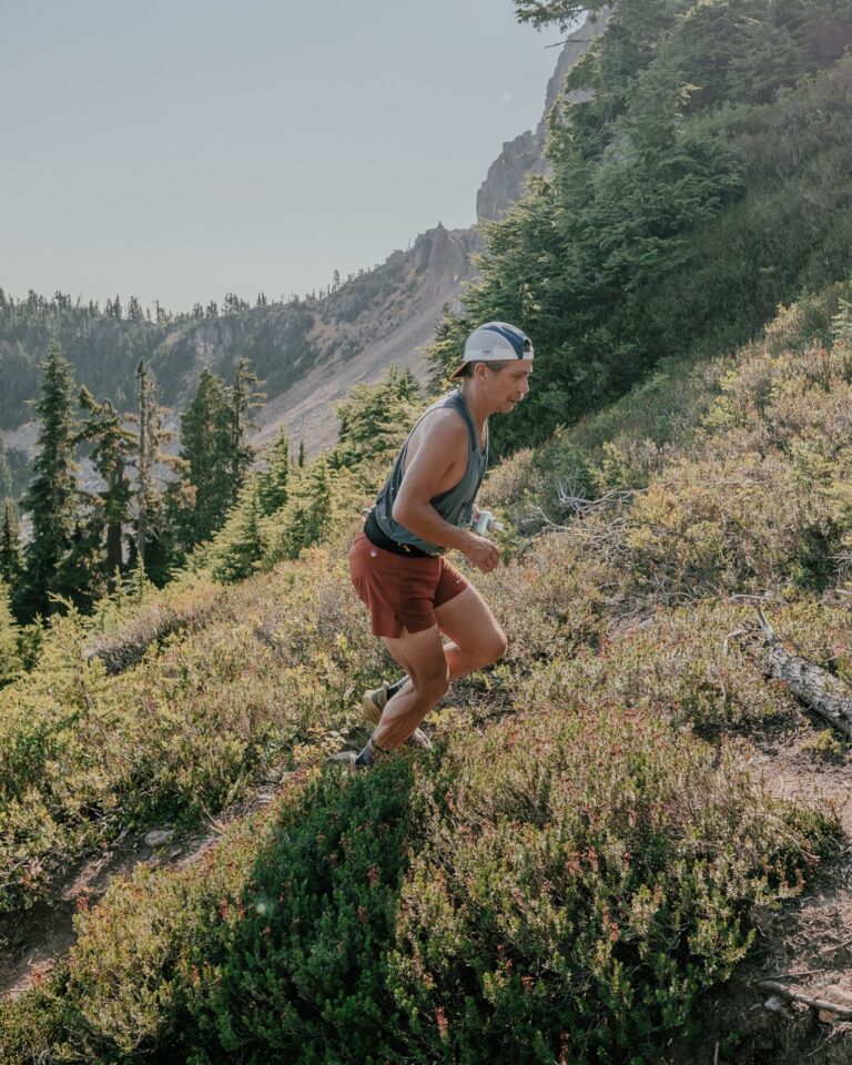 Jacob Haas running uphill on a technical mountain trail through alpine vegetation on Vancouver Island